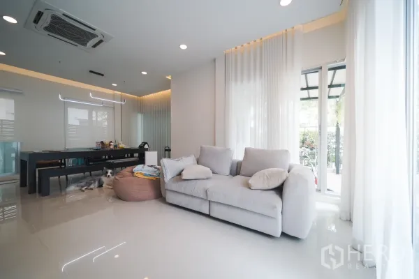 Detached House for rent or sale in Saphan Sung, Bangkok - Bright living room with large windows, sheer curtains and a plush gray sofa opening to the patio.