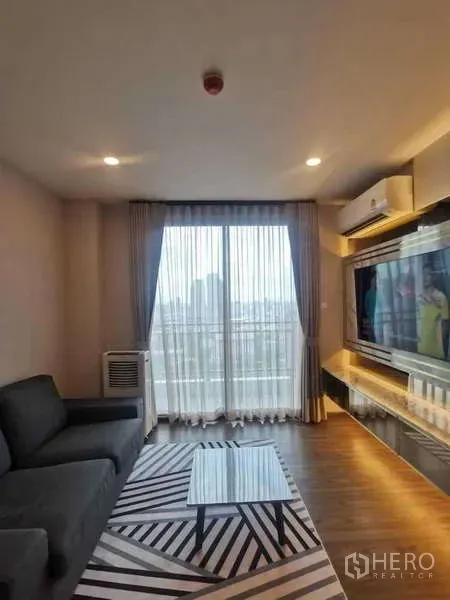 公寓 出售在Huai Khwang, Bangkok - 客厅另一视角：沙发、电视柜、纱帘与阳台外城市景观。