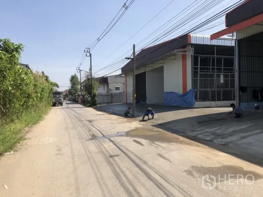 คลังสินค้า ให้เช่าในBang Kapi, Bangkok - มุมมองด้านหน้าถนนของโกดังพร้อมประตูม้วนและลานคอนกรีตบนซอยเงียบในเขตบางกะปิ กรุงเทพฯ