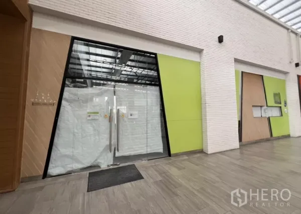 Retail Space for rent in Khlong Toei, Bangkok - Glass-fronted retail unit with double doors in a modern community mall corridor with green accent panels and skylight ceiling.