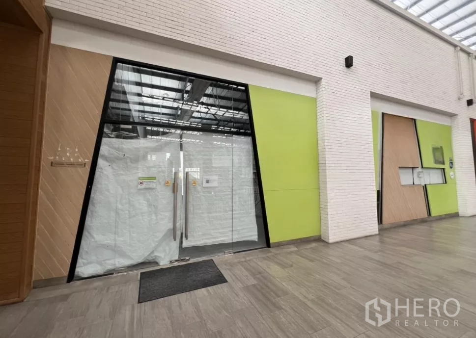 Retail Space for rent in Khlong Toei, Bangkok - Glass-fronted retail unit with double doors in a modern community mall corridor with green accent panels and skylight ceiling.