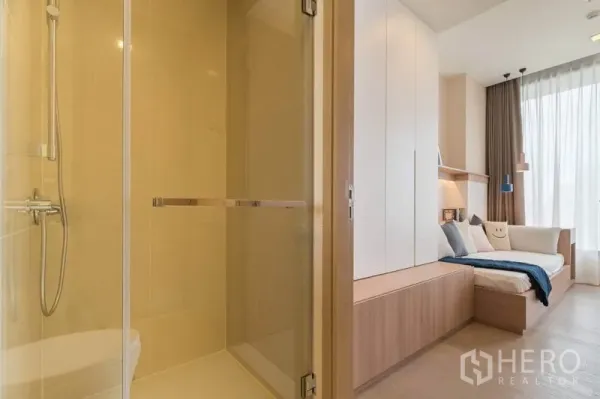公寓 出租在Watthana, Bangkok - 玻璃淋浴间旁是温馨卧室，内置衣柜与窗边日间床，高挑窗帘。