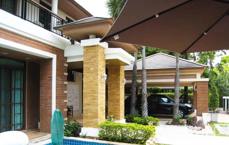 Detached House for rent or sale in Bang Phli, Samut Prakan - Facade with stone pillars, carport and landscaped garden beside the terrace.