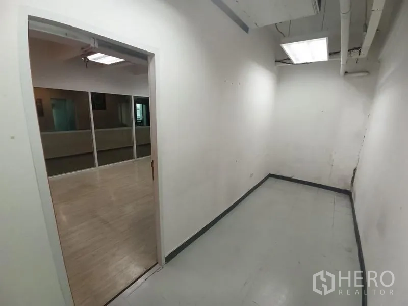 Office Space for rent in Ratchathewi, Bangkok - Narrow white anteroom leading to a glass-partitioned office with fluorescent ceiling lights.
