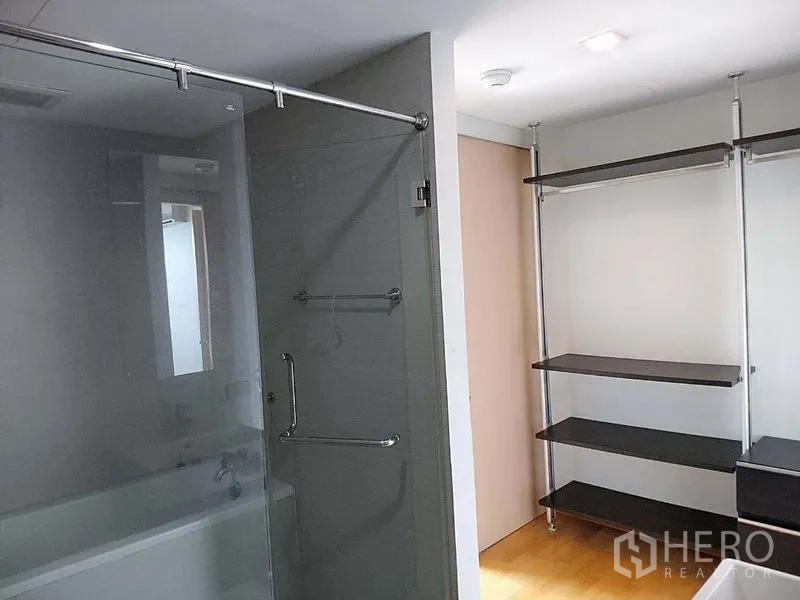 Condominium for sale in Khlong Toei, Bangkok - Bathroom with glass-enclosed bathtub and adjacent open-shelving wardrobe.