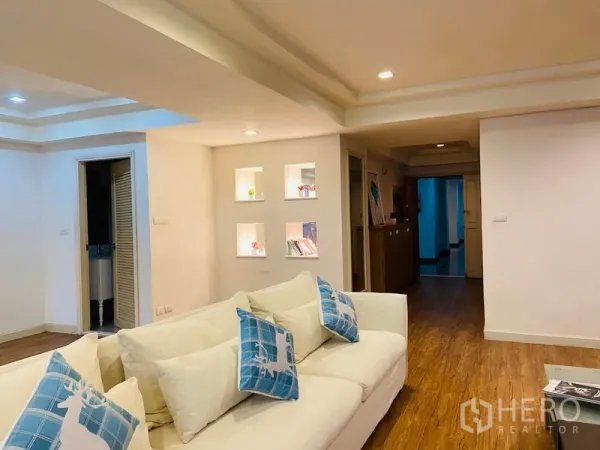 คอนโด ให้เช่าในWatthana, Bangkok - ห้องนั่งเล่นอบอุ่นด้วยโซฟาสีขาว และช่องโชว์มีไฟติดผนังบริเวณโถงทางเดินบนพื้นไม้