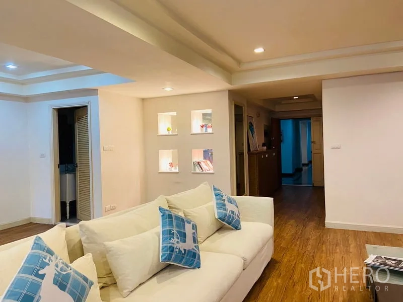คอนโด ให้เช่าในWatthana, Bangkok - ห้องนั่งเล่นอบอุ่นด้วยโซฟาสีขาว และช่องโชว์มีไฟติดผนังบริเวณโถงทางเดินบนพื้นไม้