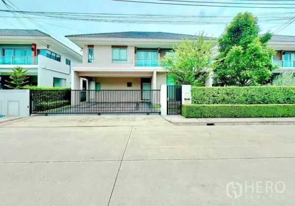 Detached House for sale in Lat Krabang, Bangkok - Front elevation of the two-storey house with black metal gate and greenery.