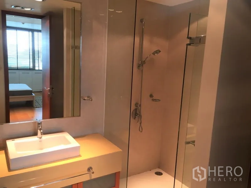 Condominium for rent in Khlong Toei, Bangkok - Modern bathroom with a glass-enclosed shower, single vanity and wall mirror.