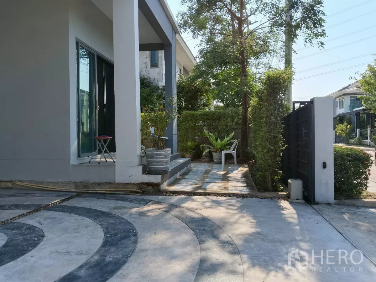 独立式住宅 出售在Lat Krabang, Bangkok - 前院露台与车道，修剪整齐的绿篱与安全大门。