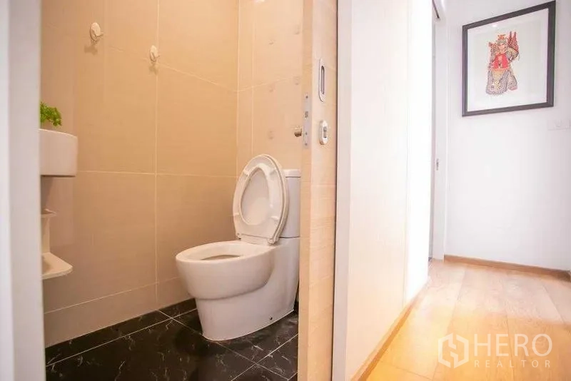 Condominium for sale in Khlong Toei, Bangkok - Clean bathroom with beige tiles, white toilet, and black marble floor.