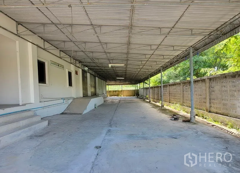 Warehouse for rent in Sam Phran, Nakhon Pathom - Long covered loading bay with metal roof, concrete driveway, ramps and multiple roller shutters.
