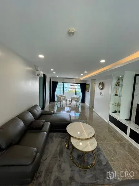 Condominium for rent or sale in Watthana, Bangkok - Open-plan living area with leather sofa, marble coffee tables and full-height windows.