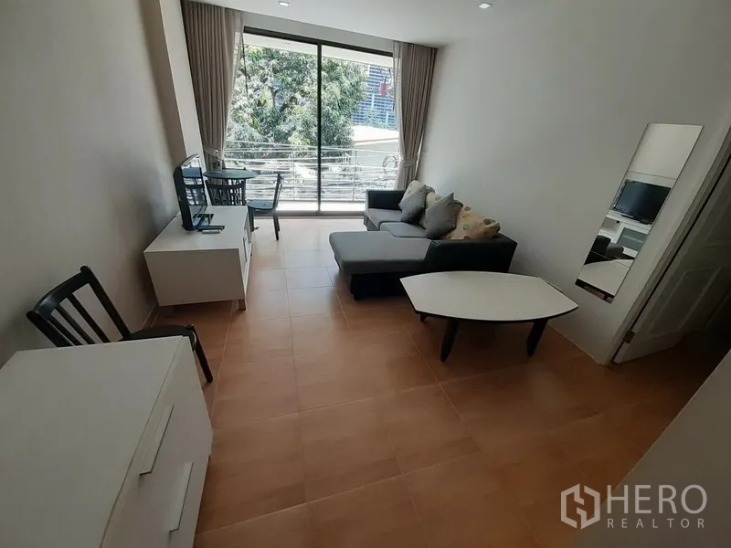 公寓 出租在Pathum Wan, Bangkok - 采光良好的客厅，转角沙发、电视柜、书桌，落地玻璃门通往阳台