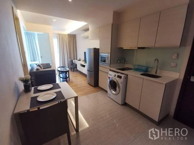 Condominium for rent or sale in Watthana, Bangkok - Kitchen and living layout featuring tall cabinets, refrigerator, TV console and wood flooring.