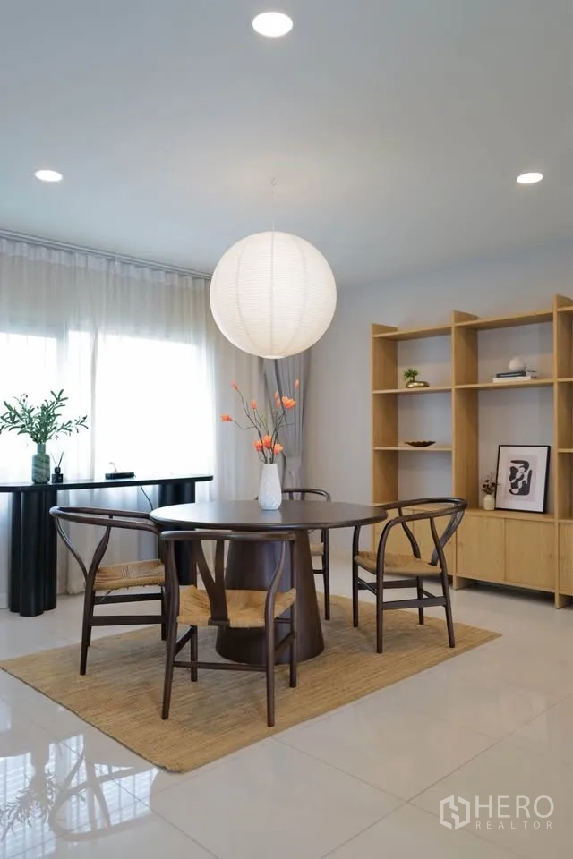 Detached House for rent or sale in Bang Phli, Samut Prakan - Bright dining area with round wooden table, wicker chairs, and a paper pendant light by a large window.