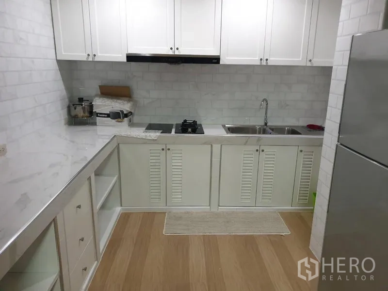 Condominium for rent in Watthana, Bangkok - Separate white kitchen with ample cabinets, hob, hood, double sink, and refrigerator.