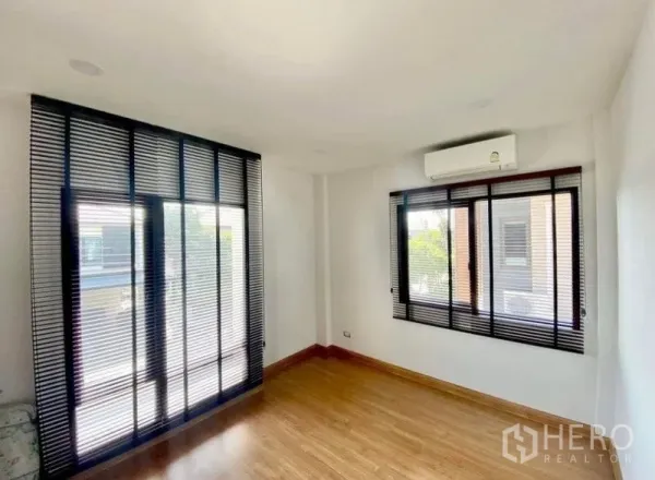 Detached House for rent - Bright empty bedroom with wood flooring, large windows with black blinds, and wall-mounted air conditioner.