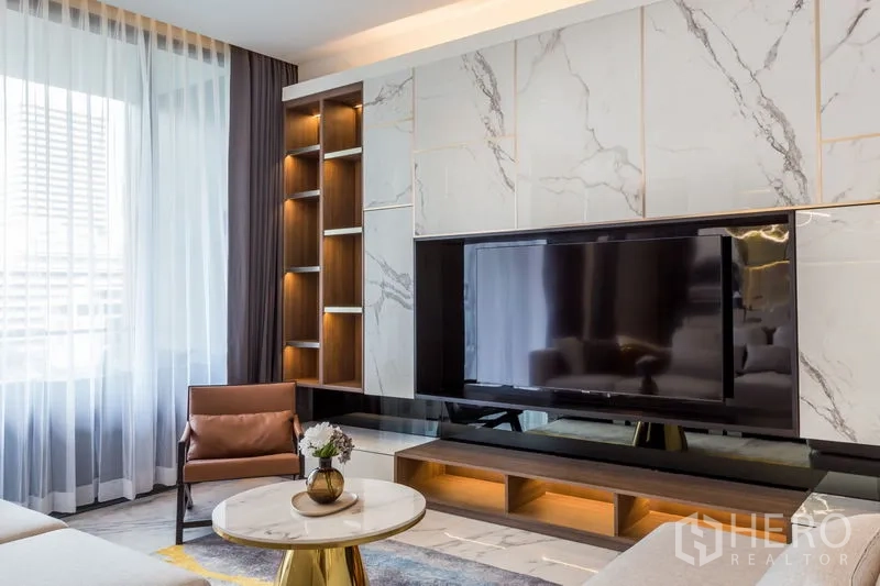 Condominium for rent in Khlong Toei, Bangkok - Living room with marble feature wall, built-in shelving and large TV.