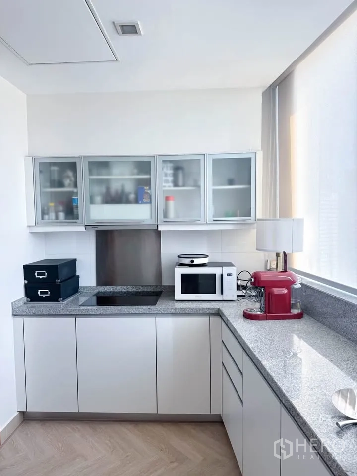 Condominium for rent or sale in Khlong Toei, Bangkok - Corner kitchen with glass-front cabinets, induction cooktop, microwave, and small appliances.