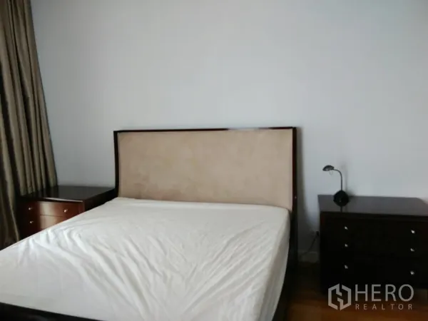 Condominium for rent in Khlong Toei, Bangkok - Bright bedroom with upholstered headboard, bedside tables, and floor-to-ceiling curtains.