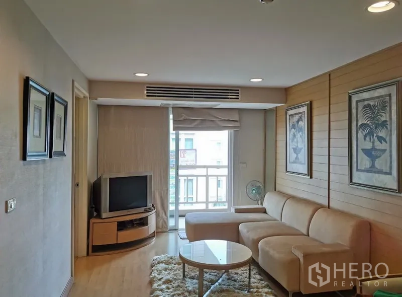Condominium for sale in Sathon, Bangkok - Bright living room with beige L-shaped sofa, TV console, wall art and sliding door to a small balcony in a Sathon condo.
