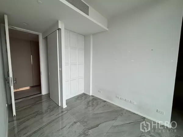 Condominium for sale in Bang Kho Laem, Bangkok - Empty room with white paneled wall, sliding door and glossy grey marble flooring with multiple power outlets.