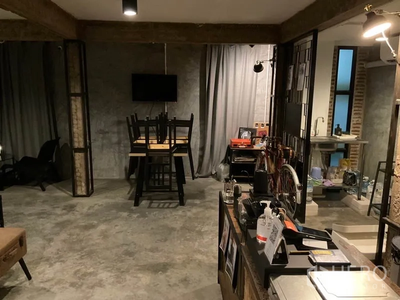 Home Office for rent in Phaya Thai, Bangkok - Industrial-style workspace with concrete floor, curtained wall, stacked chairs on a table, bicycle storage and a small kitchenette with sink.