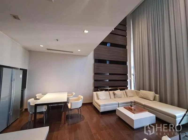 公寓 出租或出售在Huai Khwang, Bangkok - 开放式客餐厅，L形沙发、木地板与高挑窗帘。