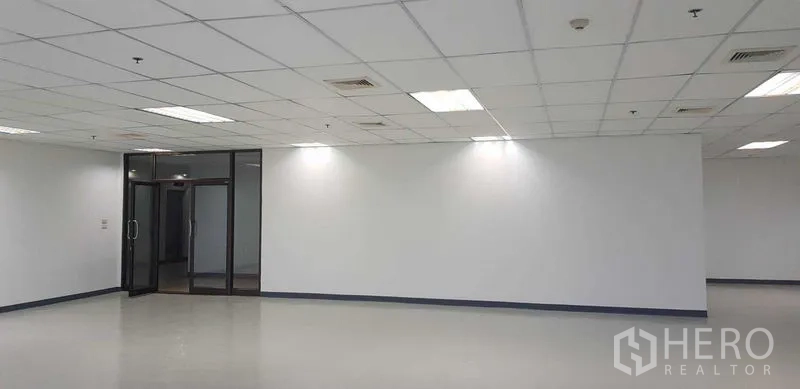 Office Space for rent in Khlong Toei, Bangkok - Empty office floor with glass entry, clean white walls, recessed lighting and air-conditioning vents.
