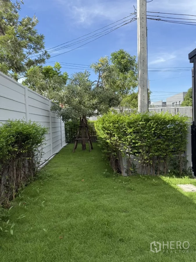 Townhouse for rent or sale in Bang Phli, Samut Prakan - Lush side garden with hedges and trees along a white privacy fence.