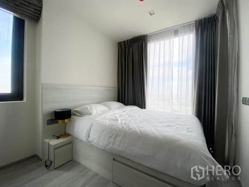 Condominium for rent in Phra Khanong, Bangkok - Sunlit bedroom with large bed, sheer curtains and expansive city view from a floor-to-ceiling window.