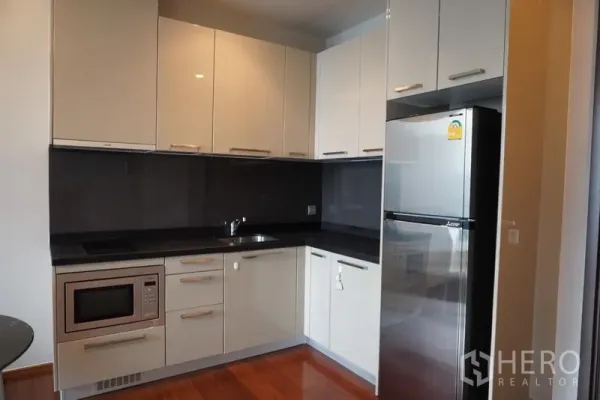 Condominium for rent in Watthana, Bangkok - Modern L-shaped kitchen with glossy cabinets, cooktop, microwave and stainless fridge at Quattro by Sansiri.