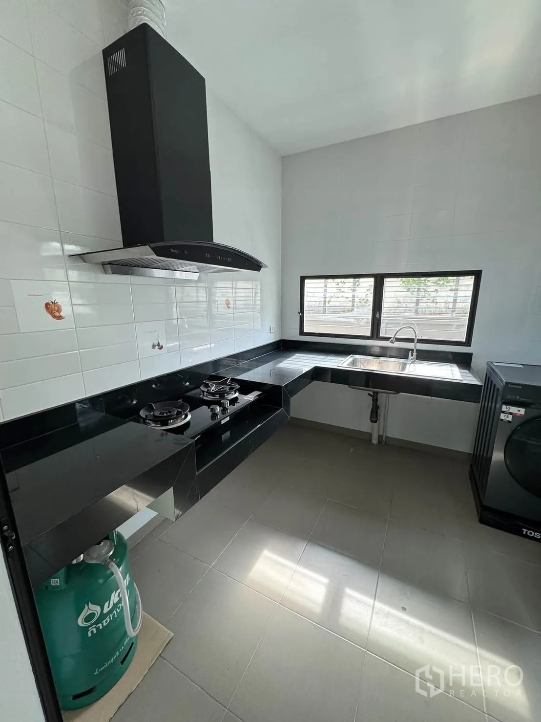 Detached House for rent in Prawet, Bangkok - Separate kitchen with gas hobs, range hood, black countertops, sink, and a washer.