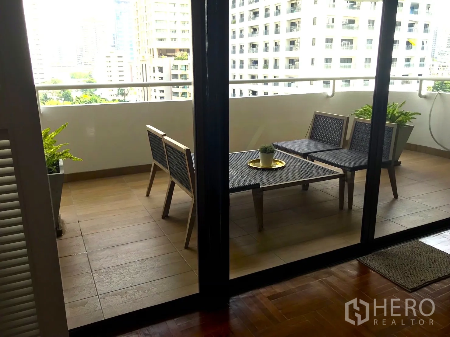 Condominium for rent in Bangkok - Covered balcony with outdoor table and chairs overlooking nearby buildings.