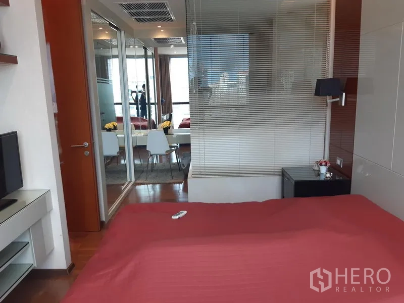 Condominium for rent in Khlong Toei, Bangkok - Bedroom interior with red bedspread, glass partition, and mirrored wardrobe.