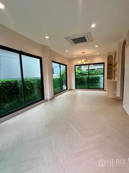 Detached House for sale in Bang Kruai, Nonthaburi - Bright living and dining area with floor-to-ceiling sliding glass doors, herringbone flooring, cassette AC and garden view.
