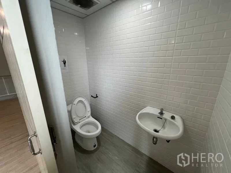 Warehouse for rent in Prawet, Bangkok - Clean restroom finished with white subway tiles, toilet and wall-mounted sink.