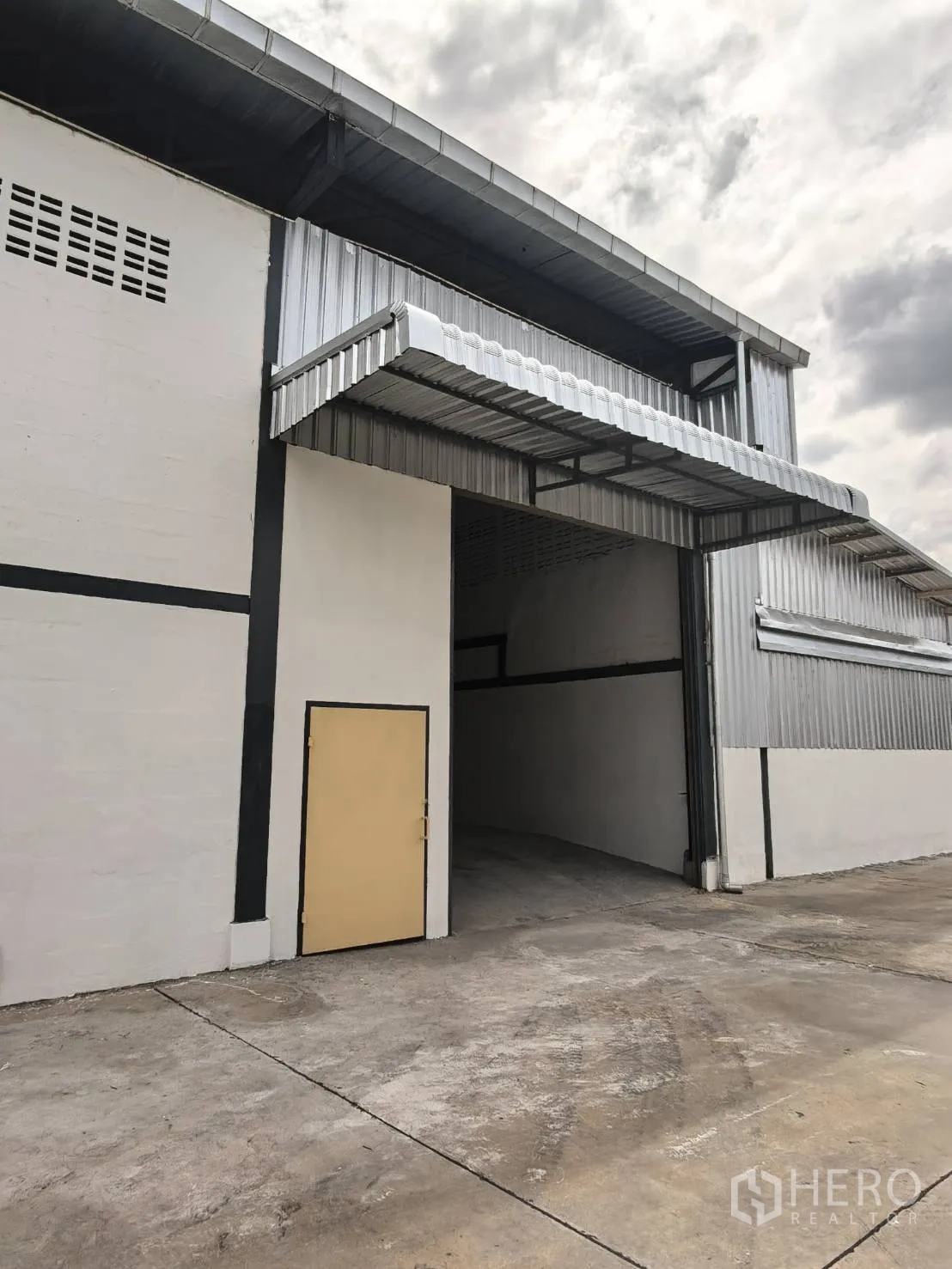 โกดัง for rent in Suan Luang, Bangkok - ด้านหน้าโกดังผนังเมทัลชีท มีชายคาคลุมจุดขนถ่ายและช่องทางเข้าขนาดสูง พร้อมพื้นคอนกรีต.
