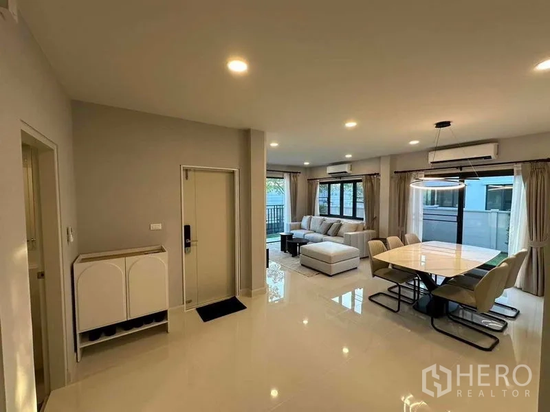 Detached House for rent in Bang Phli, Samut Prakan - Open-plan living and dining area with glossy tile floors, L-shaped sofa, large windows and sliding glass doors.