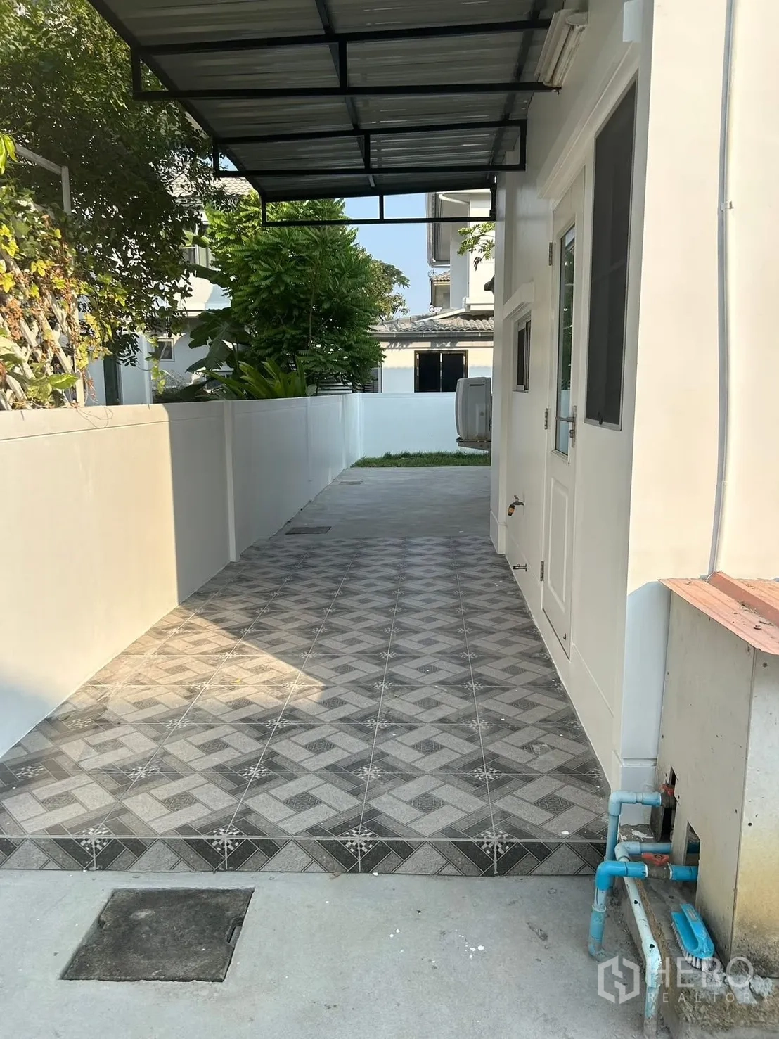 Detached House for rent in Bang Na, Bangkok - Side walkway under a metal canopy with patterned tiles and utility access.