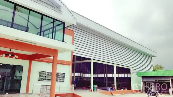 Factory for sale in Pathum Thani - Factory facade showing corner glass office and open loading bay beneath a metal roof.