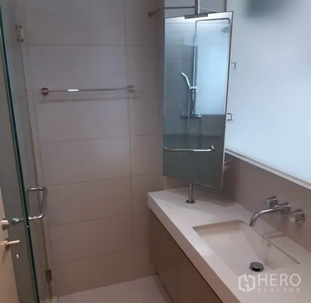 Condominium for rent in Khlong Toei, Bangkok - Contemporary bathroom featuring a long vanity, wall mirror and a glass-enclosed shower.