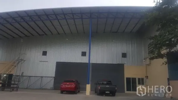 Factory for rent in Khlong Luang, Pathum Thani - Steel-clad factory exterior in Khlong Luang with high roof canopy, roller shutter door, and front parking area.