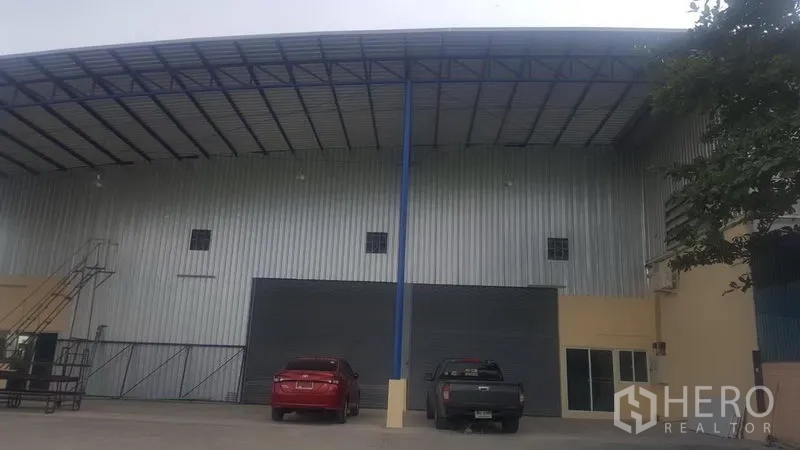 Factory for rent in Khlong Luang, Pathum Thani - Steel-clad factory exterior in Khlong Luang with high roof canopy, roller shutter door, and front parking area.