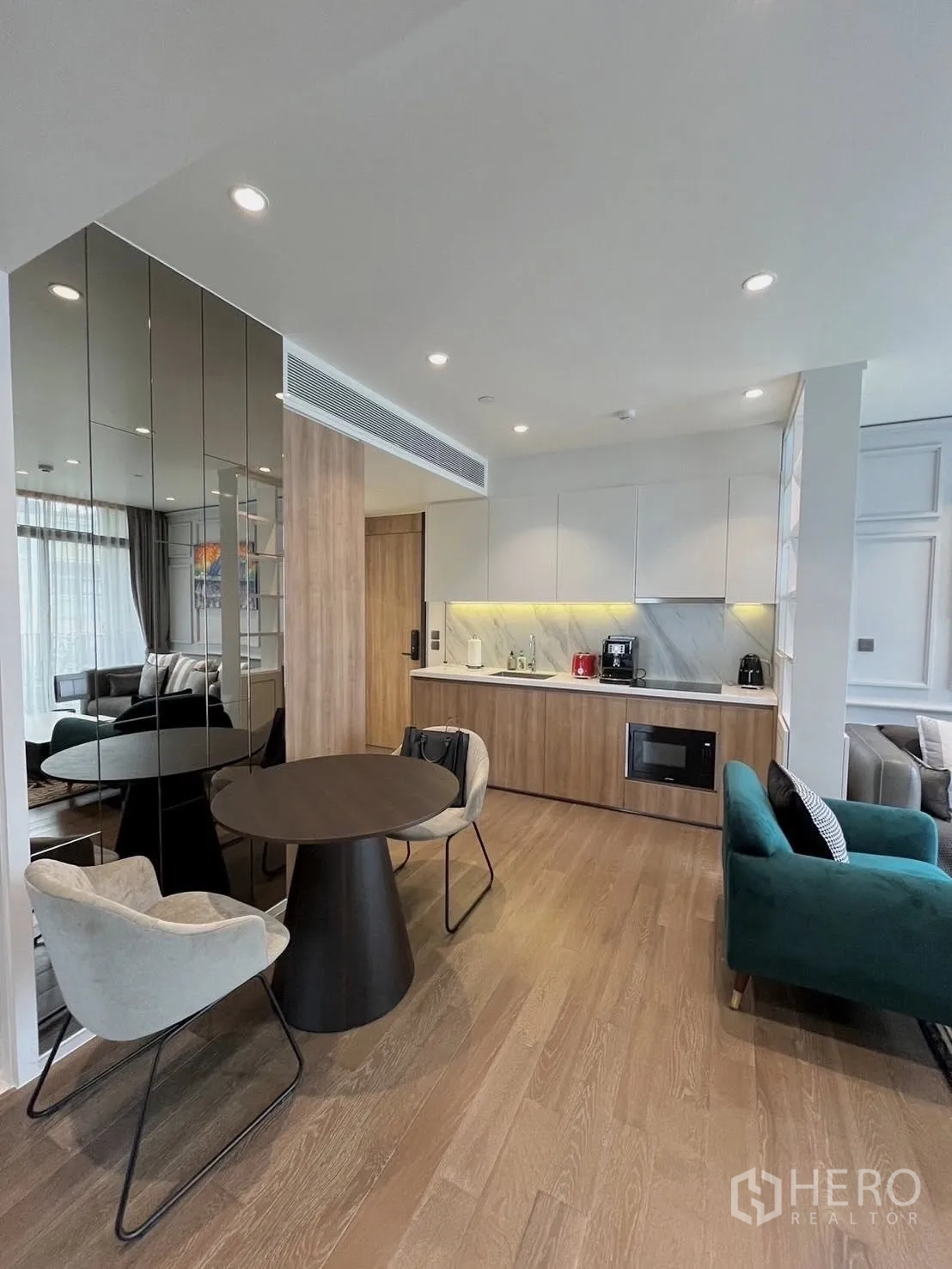 คอนโด for rent in Watthana, Bangkok - พื้นที่นั่งเล่นแบบเปิดโล่งพร้อมโต๊ะทานอาหารทรงกลม ผนังกระจกเงา พื้นไม้ ครัวบิลท์อิน และโซฟาสีเขียวอมฟ้า