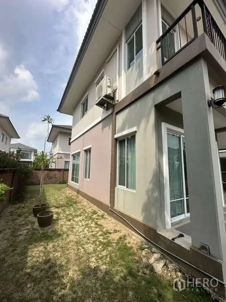 Detached House for sale in Sai Mai, Bangkok - Side yard with grass, potted plants and a glass door entrance.