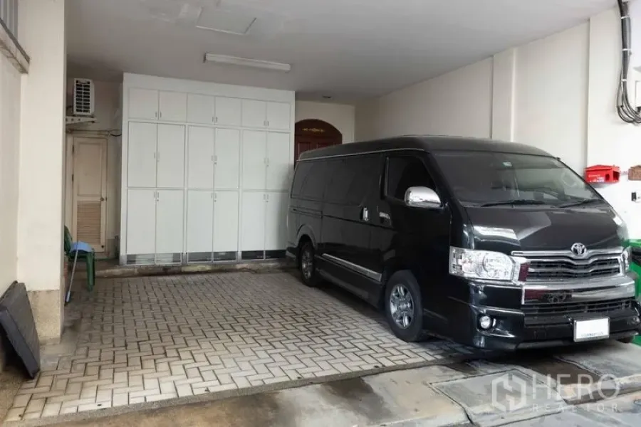 Townhouse for sale - Covered carport with brick paving, white storage cabinets and a parked van.