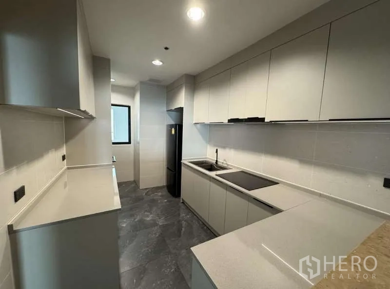 Condominium for rent - Renovated galley kitchen with stone-tile floor, sleek white cabinetry, fridge and induction cooktop.