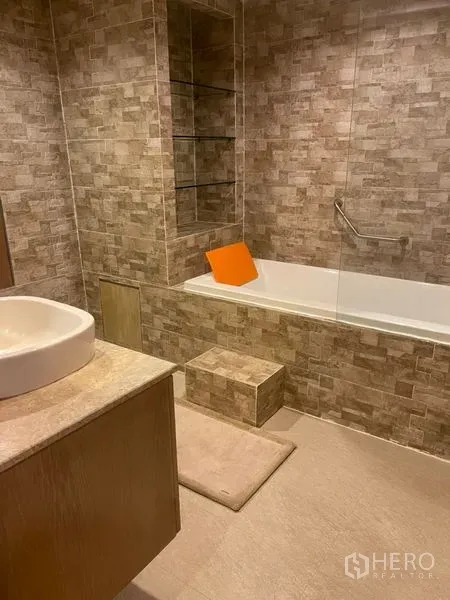 Townhouse for rent in Suan Luang, Bangkok - Contemporary bathroom with stone tiles, built-in shelving, vanity and bathtub with glass screen.